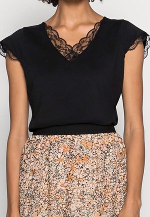 Czarny krótki top z koronkowym dekoltem w kształcie litery V, zestawiony z kwiecistą spódnicą w delikatnych odcieniach pomarańczu i kremu, z marszczonym paskiem w talii.