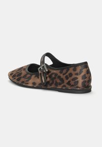 Chaussures plates à imprimé léopard avec une finition douce semblable à du daim, des bords noirs et un détail de sangle réglable sur le côté.