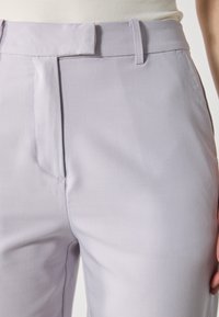 Světle levandulové kalhoty s hladkou texturou, mají elegantní siluetu, plochý přední díl a poutka na opasek. Viditelné minimální prošívání.
