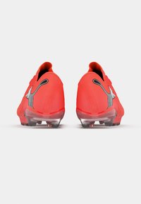 Botas de fútbol rojas con parte superior texturizada, logotipo destacado y tacos transparentes para tracción. Diseñadas sin cordones, con una forma aerodinámica.