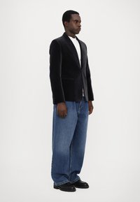 Juoda aksominė švarka su iškirptėmis, dėvima ant baltos marškinėlių. Derinama su plačiais mėlynais džinsais ir juodais dideliais batais.