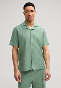 Camicia a maniche corte con colletto in tessuto verde chiaro testurizzato, caratterizzata da una chiusura con bottoni e una vestibilità comoda.