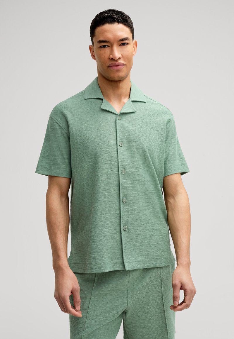 Camicia a maniche corte con colletto in tessuto verde chiaro testurizzato, caratterizzata da una chiusura con bottoni e una vestibilità comoda.