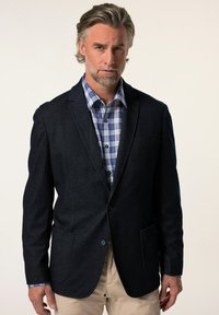 Marinblazer i strukturerad tyg med två framfickor, kombinerad med en blårutig skjorta med knapplås.
