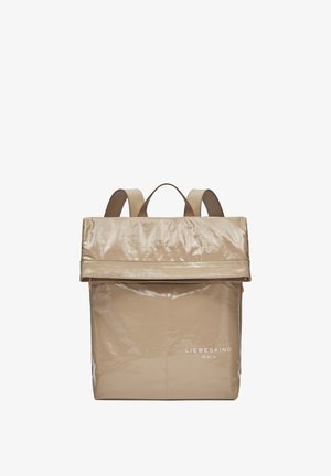 Sac à dos pliable beige en matériau brillant, présentant une forme rectangulaire simple, deux bretelles et un logo blanc à la base.