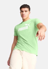 T-shirt verde chiaro realizzato in cotone, con un grande logo bianco "PUMA" e un piccolo accento del logo. Design a maniche corte e scollo rotondo.