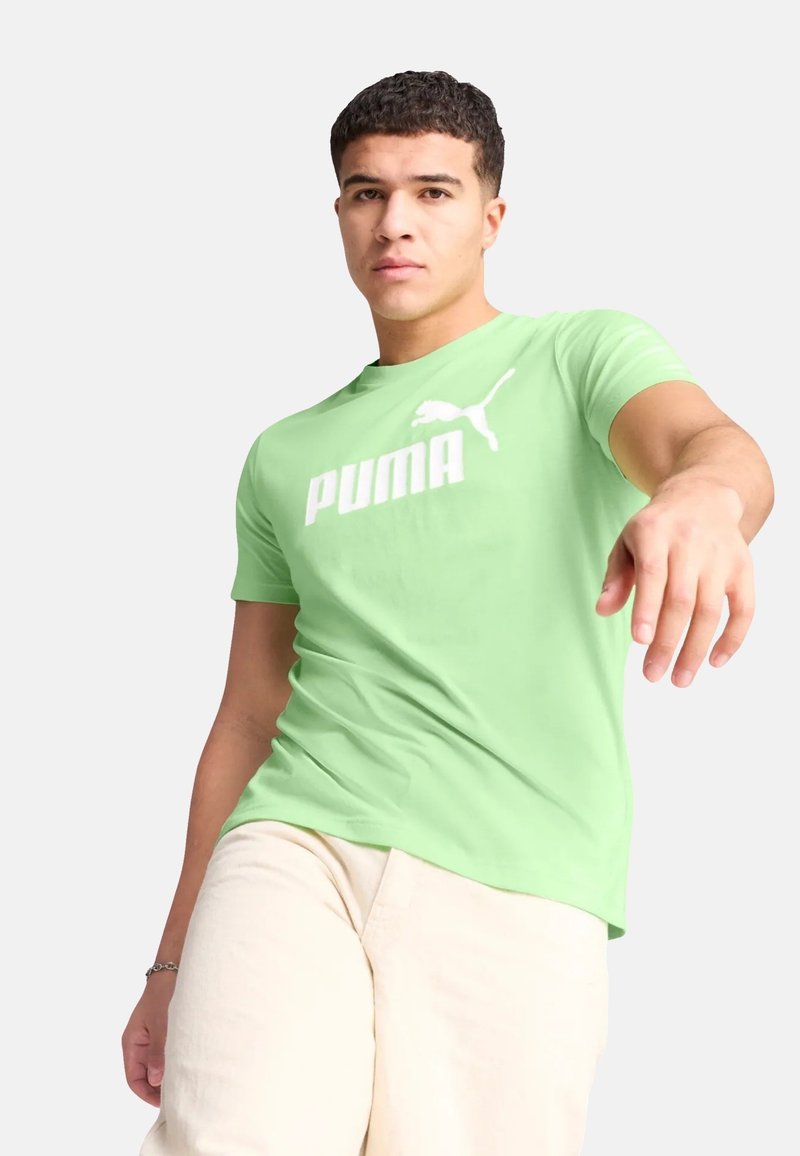T-shirt verde chiaro realizzato in cotone, con un grande logo bianco "PUMA" e un piccolo accento del logo. Design a maniche corte e scollo rotondo.