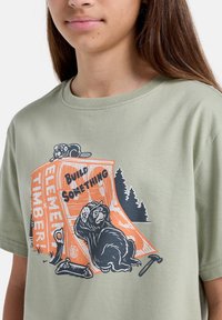 Oliven grøn bomulds t-shirt med korte ærmer, prydet med et grafisk design af dyr og teksten "Byg noget" i orange.