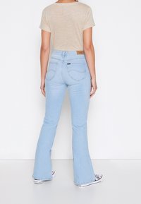 Jeans de campana en azul claro con cintura alta, con bolsillos y costuras en contraste, combinados con una camiseta de manga corta en color beige.