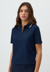 Marineblauw polo shirt met korte mouwen, ritskraag en witte accentdetails op de kraag. Zachte, gladde stof met een losse fit.