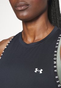 Top atlético sin mangas negro hecho de una tela suave, con un logo y marca en blanco a lo largo de las costuras de los hombros en un diseño contrastante.