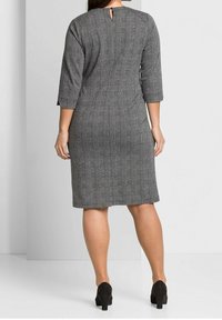 Robe à carreaux gris avec manches trois-quarts, longueur au genou, et ouverture en forme de goutte d'eau dans le dos. Tissu lisse avec une coupe structurée.