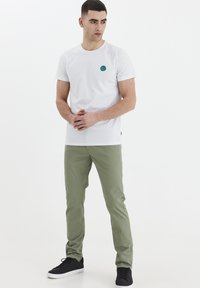 Hvit bomulls t-skjorte med en liten blå og grønn sirkulærlogo, parret med lysegrønne bukser og svarte joggesko.