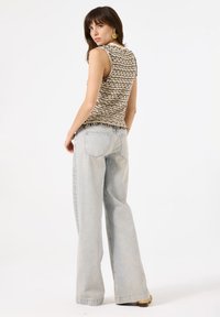 Stricktop mit einem strukturierten schwarz-weißen Muster, kombiniert mit hellblauen weit geschnittenen Jeans. Der fransige Saum des Tops fügt ein Detail hinzu.