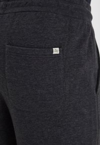Pantalon de survêtement gris foncé en tissu doux, doté d'une poche arrière avec une petite étiquette tissée. Texture lisse et conception à coupe décontractée.