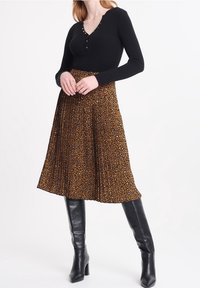 Svart, ribbad långärmad topp med knapprad, i kombination med en knälång brun plisserad kjol med leopardmönster. Svarta knähöga stövlar.