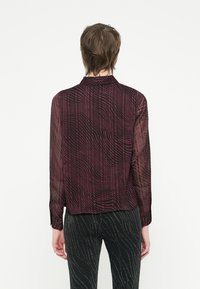 Camicia trasparente a maniche lunghe di un profondo bordeaux con un motivo a strisce ondulate, dotata di un colletto e polsini con bottoni.