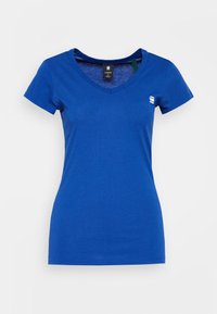 Blå kortärmad V-ringad T-shirt för kvinnor med en liten vit logotyp på vänster bröst och en svart storlekslapp inne i kragen.