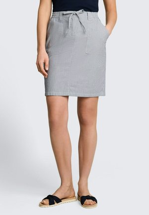 Kobieta nosząca jasnoszarą spódnicę do kolan z przednimi kieszeniami i wiązanym paskiem w talii, zestawioną z czarnymi sandałami na płaskiej podeszwie.