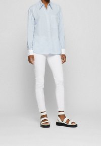 Světle modrá pruhovaná košile s knoflíky, bílé slim-fit džíny a bílé sandály s černou platformou.