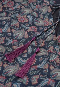 Navy bloemenpatroon stof met roze en teal motieven, voorzien van paarse franjes en gevlochten banden. Zachte textuur met ingewikkelde details.