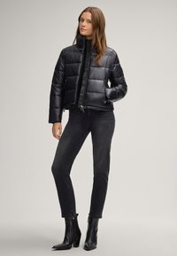 Giacca a vento nera con colletto alto e chiusura con zip, caratterizzata da un motivo trapuntato. Indossata con jeans scuri e stivaletti neri.