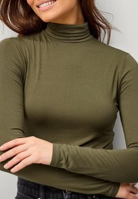 Olivenfarbener Rollkragenpullover aus weichem, dehnbarem Stoff mit langen Ärmeln und körpernaher Passform. Glatte Textur und dezente Nahtdetails.