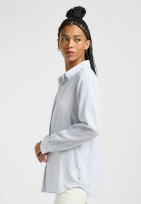 Hellblau-weiß gestreiftes Langarmhemd mit Button-Down-Kragen, weicher Textur und abgerundetem Saum. Verfügt über Knöpfe an den Manschetten und seitliche Schlitze.