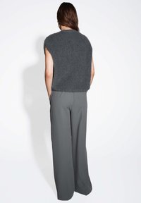 Haut en tricot sans manches gris avec une finition texturée et un ourlet irrégulier, associé à un pantalon gris à larges jambes. Les tissus semblent doux et fluides.