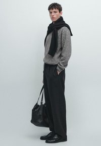 Maglione grigio in lanaviscosa, sciarpa nera in maglia, pantaloni neri a vita alta, scarpe nere in pelle e una borsa a spalla nera in pelle. Sfondo neutro.