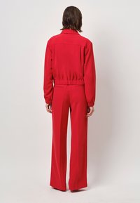 Rode two-piece outfit met een aansluitende jas met een elastische taille en lange mouwen, gecombineerd met wijde broekspijpen. Soepele textuur.