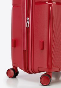 Maleta rígida roja con superficie texturizada, cremalleras dobles y ruedas redondeadas. Cuenta con un asa lateral y un acabado suave.