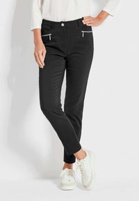 Schwarze Hose im Slim-Fit-Stil mit zwei Reißverschlusstaschen auf der Vorderseite, aus einem glatten Stoff gefertigt. Kombiniert mit weißen Sneakers.