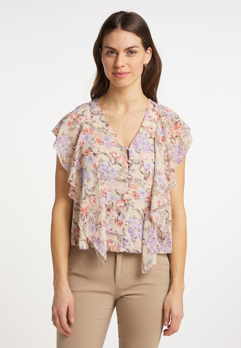 Blusa floreale con scollo a V, maniche arricciate e bottoni. Il motivo include fiori rosa e viola su uno sfondo beige.