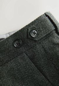 Gray herringbone fabric with a smooth texture, featuring two black buttons at the waistband and a folded edge visible in the foreground.