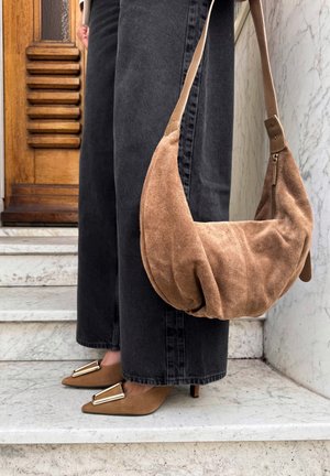 Braune Wildlederhandtasche mit einem lässigen Design und einem Ledertragegurt. Kombiniert mit dunkelgrauen, weit geschnittenen Jeans und spitzen Absatzschuhen mit goldenen Akzenten.