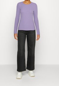 Paars ribbelshirt met lange mouwen, gecombineerd met zwarte flared jeans en witte sneakers, met een ronde hals en een getailleerde snit.