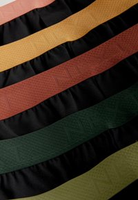 Dažādkrāsaini auduma joslas ar maiņām melniem un rakstainiem krāsainiem svītrainēm rūsas, zeltainā un zaļā krāsā, ar reljefu zīmolu.