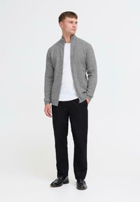 Szary sweter na zamek wykonany z miękkiego materiału, z wysokim kołnierzem i ściągaczami przy mankietach, w połączeniu z czarnymi spodniami i czarnymi butami.