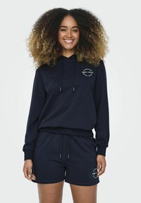 Felpa con cappuccio blu navy con lacci e logo frontale, abbinata a pantaloni corti coordinati, entrambi in tessuto morbido e con una vestibilità rilassata.