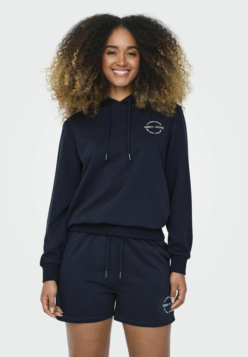 Felpa con cappuccio blu navy con lacci e logo frontale, abbinata a pantaloni corti coordinati, entrambi in tessuto morbido e con una vestibilità rilassata.