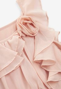 Tissu rose doux avec un délicat détail de rose à volants et des volants en cascade superposés sur un tissu léger à texture pour robe.