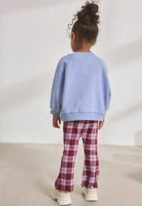 Blå sweatshirt med raglanärmar, kombinerad med bordeauxrutiga byxor med lila linjer och scallopkant. Vita sneakers.