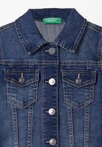 Giacca di jeans blu scuro con colletto a punta, quattro bottoni metallici sul davanti, due tasche sul petto con pattina e bottone, e etichetta verde United Colors of Benetton.