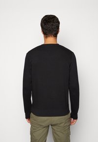 Felpa nera con maniche lunghe, polsini e orlo a costine, design a girocollo, realizzata in un mix di cotone testurizzato.