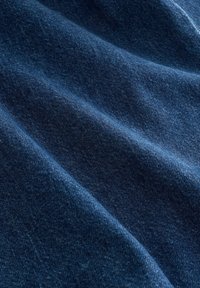 Tissu en denim bleu foncé avec une texture visible et des plis diagonaux créant des ombres douces et des reflets.