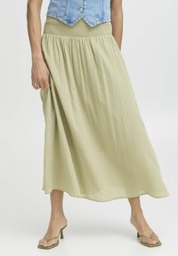Jupe fluide vert clair en tissu texturé avec taille smockée. Associée à des sandales à talons hauts vertes.