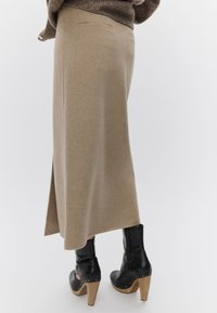 Μπεζ μάλλινη φούστα μέσης μήκους με πλευρική σχισμή, διακοσμημένη με δύο πίσω τσέπες. Συνδυάζεται με μαύρα μποτάκια πλατφόρμας με ξύλινα τακούνια.