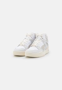 High-top sneakers in white leather with beige suede accents. Features include a padded collar, perforated detailing, and thick rubber sole.