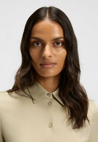 Beige Hemd mit Kragen und Knöpfen, glatte Textur und taillierte Passform, mit spitzem Kragen und minimalistischer Gestaltung.